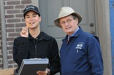 two men standing next to each other in front of a building with a clipboard