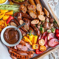 an assortment of sausages, peppers, and other foods on a tray with dipping sauce