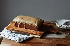 a loaf of cake sitting on top of a wooden cutting board next to a knife and fork