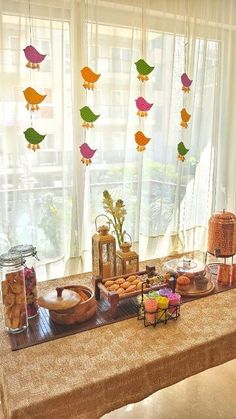 a long table with food and decorations on it in front of a window that has birds hanging from the windowsill