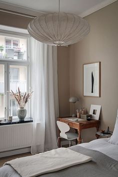 a bed sitting under a window next to a white table and chair in a bedroom