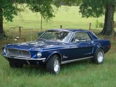 an old blue mustang sitting in the grass