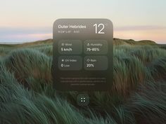 an iphone screen showing the weather and time in front of a grassy field at sunset