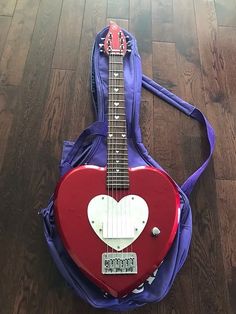 a red and white guitar with a heart on it's back case sitting on the floor