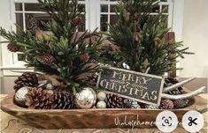 a wooden tray filled with pine cones and evergreens next to a sign that says merry christmas