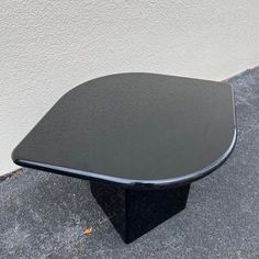 a black table sitting on top of a cement floor next to a white wall and sidewalk