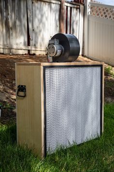 an air conditioner sitting on top of a wooden box in the grass next to a fence