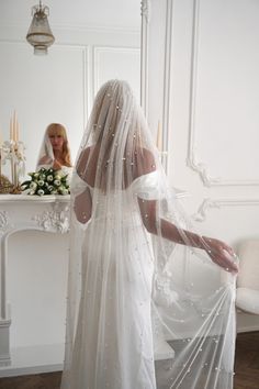 a woman in a wedding dress looking at herself in the mirror with her veil draped over her head