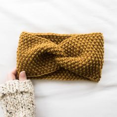 a hand holding a knitted headband on top of a white bed with sheets