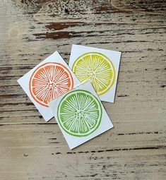 three pieces of paper cut into four different colors and shapes, each with a slice of orange in the middle