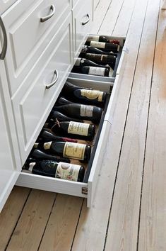 an open drawer in the middle of a kitchen with several bottles of wine on it