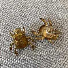 two gold colored bugs sitting next to each other on a white cloth covered surface, with one beetle facing the camera