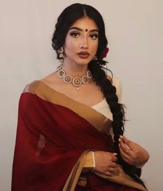 a woman wearing a red and gold sari with her hair in a fishtail braid