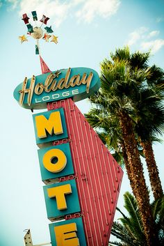 a motel sign with palm trees in the foreground and a blue sky behind it