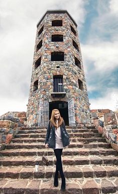 a woman standing in front of a very tall brick building with stairs leading up to it