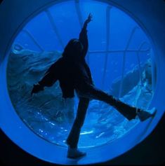 a person standing in front of an aquarium looking at the water and holding their arms up