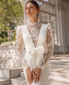 a woman in a white wedding dress with a bow at the waist and long sleeves