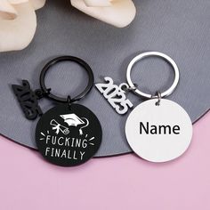 two personalized keychains are shown on a pink and gray surface with flowers