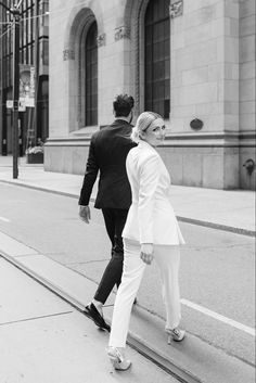 a man and woman walking down the sidewalk in front of a building on a city street