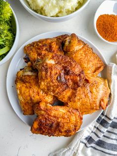 two white plates filled with chicken wings next to bowls of mashed potatoes and broccoli