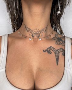 a woman with tattoos on her chest wearing a white tank top and silver hoop earrings