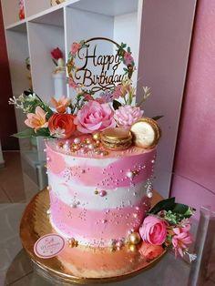 a pink and gold birthday cake with flowers on the top is sitting on a table