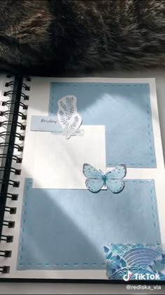 an open notebook with butterflies on it and a cat's paw next to it