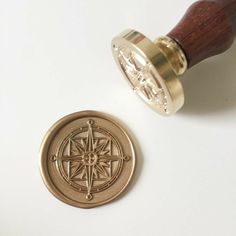 a brass stamp with a compass on it next to a wooden handle that is attached to a white surface