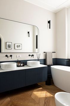 a white bath tub sitting next to a bathroom sink under a large mirror above it