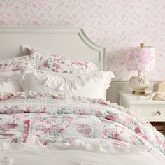 a white bed with pink flowers on the comforter and pillows in front of it