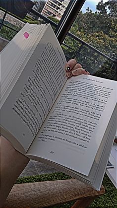 an open book sitting on top of a wooden chair in front of a glass window