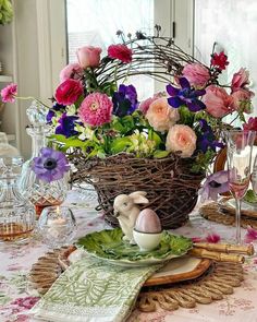 a basket filled with flowers sitting on top of a table next to wine glasses and plates