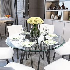 a glass dining table with white chairs and flowers in a vase on the centerpiece