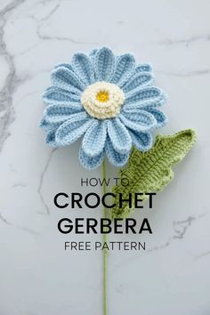 a crocheted blue flower sitting on top of a white marble counter next to a green leaf