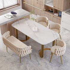 a marble dining table with gold legs and beige chairs around it in a modern kitchen