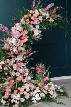 an arrangement of pink and white flowers in front of a blue door with greenery