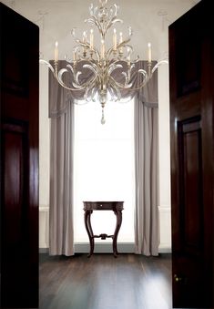 a chandelier hangs from the ceiling in front of a window with drapes