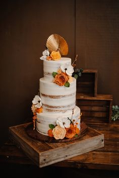 a three tiered cake with flowers and shells on top is sitting on a wooden table