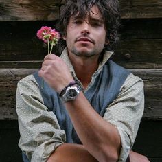 a man sitting on the ground with a flower in his hand and wearing a watch