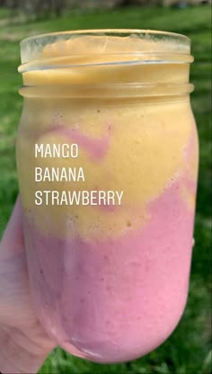 a hand holding a jar filled with fruit and yogurt on top of green grass