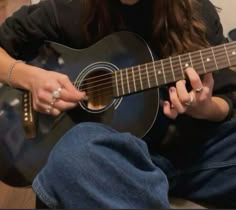 a woman is sitting on the floor playing an acoustic guitar with her hands and fingers