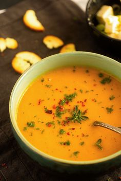 there is a bowl of soup on the table next to some crackers and bread