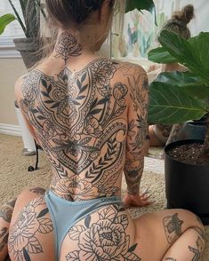 a woman with tattoos on her back sitting on the floor next to a potted plant