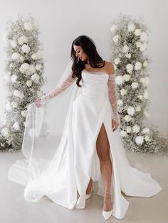 a woman wearing a white wedding dress with sheer sleeves and thigh high slits is posing for the camera