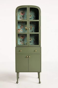 a green china cabinet with floral wallpaper on the front and bottom shelves, along with brass knobs