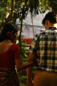 a man and woman standing next to each other in front of some trees with the sun shining on them