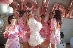 a group of women in pink robes standing next to each other with balloons behind them