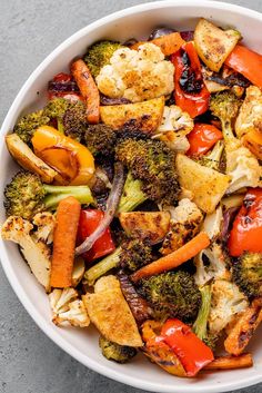 a white bowl filled with broccoli, carrots and cauliflower on top of a table