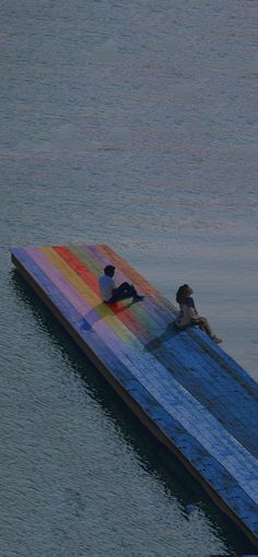 two people are sitting on a raft floating in the water with a rainbow colored cover