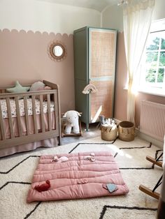 a baby's room with pink walls and rugs on the floor, including a crib